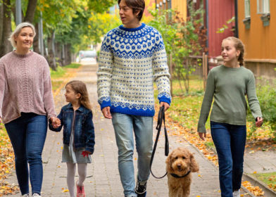 Perhe kävelee ulkona puutaloalueella.