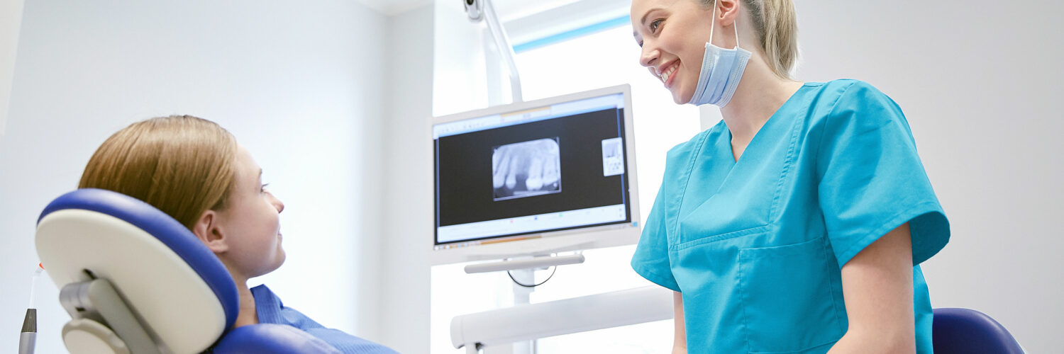 Hammaslääkäri katsoo potilasta ja näyttää röntgenkuvaa hampaasta.