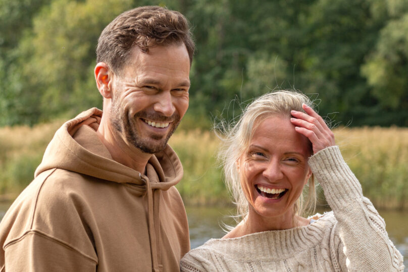 Mies ja nainen seisovat hymyillen vesistön äärellä
