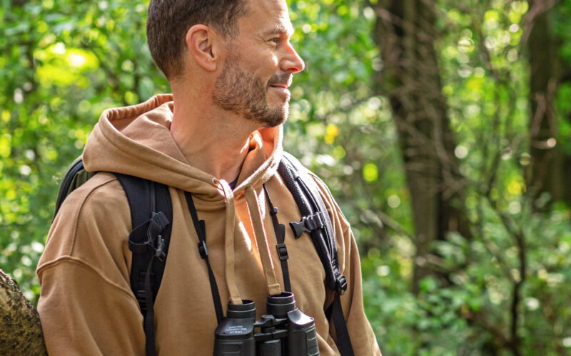 Mies katsoo sivulle kiikarit kaulassa metsässä.