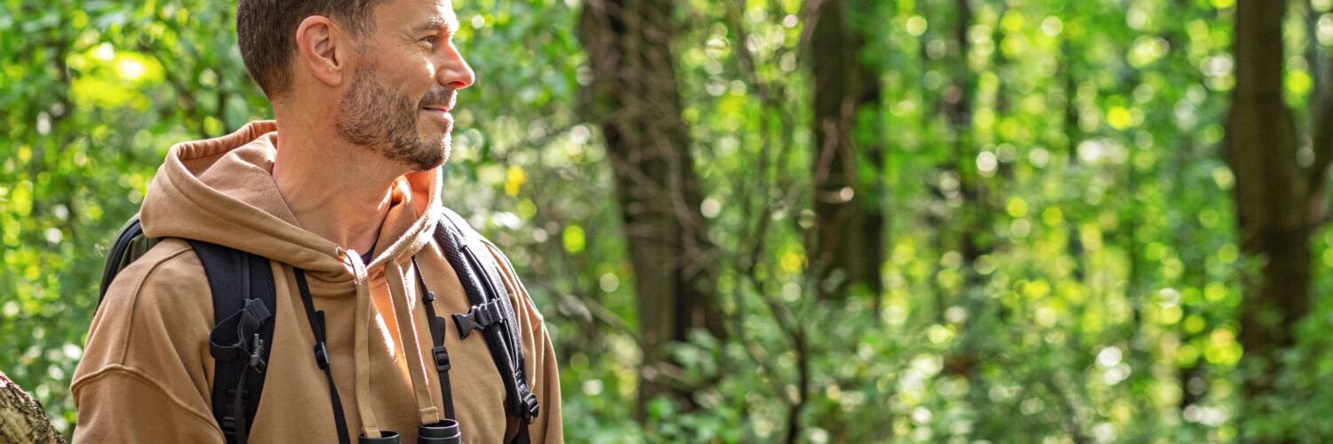 Mies katsoo sivulle kiikarit kaulassa metsässä.