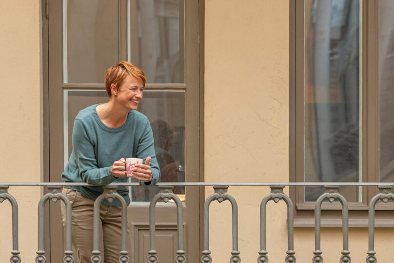 Punahiuksinen nainen nojaa terassin metallikaiteeseen.