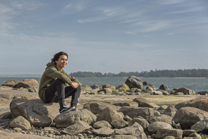 Yksinäinen nuori istuu rannalla. Älä jää yksin, jos sinulla on haastava hetki elämässä. Nuotista voit saada apua.