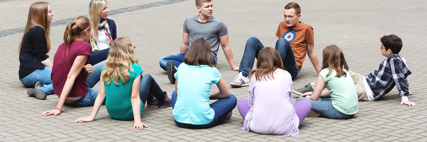 Bunch of young people sitting in a circle and talking to each others.