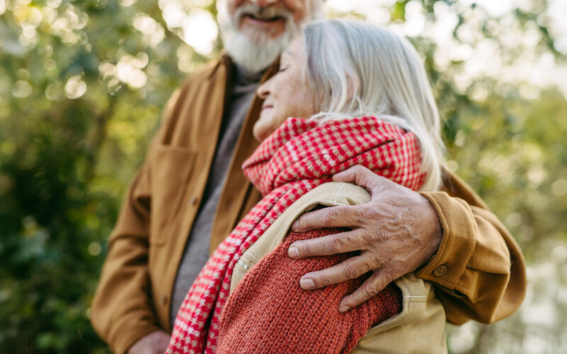 Iäkäs pariskunta nojaa toisiinsa ulkona.