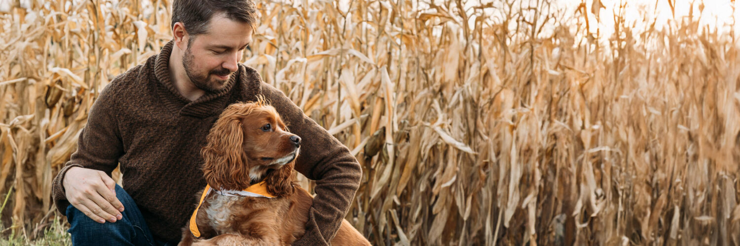 Mies ja koira istumassa pellonreunassa.