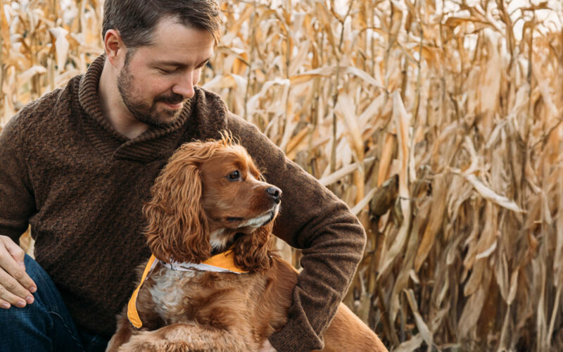 Mies ja koira istumassa pellonreunassa.