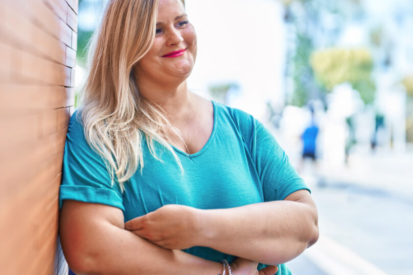 Neurologisten sairauksien moniammatillisen yksilökuntoutuksen asiakas ulkoilee ja nojailee talon seinään iloisena