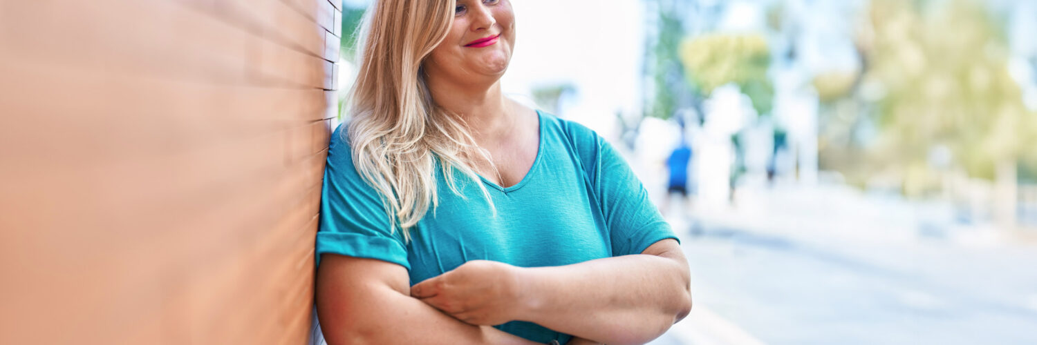 Neurologisten sairauksien moniammatillisen yksilökuntoutuksen asiakas ulkoilee ja nojailee talon seinään iloisena