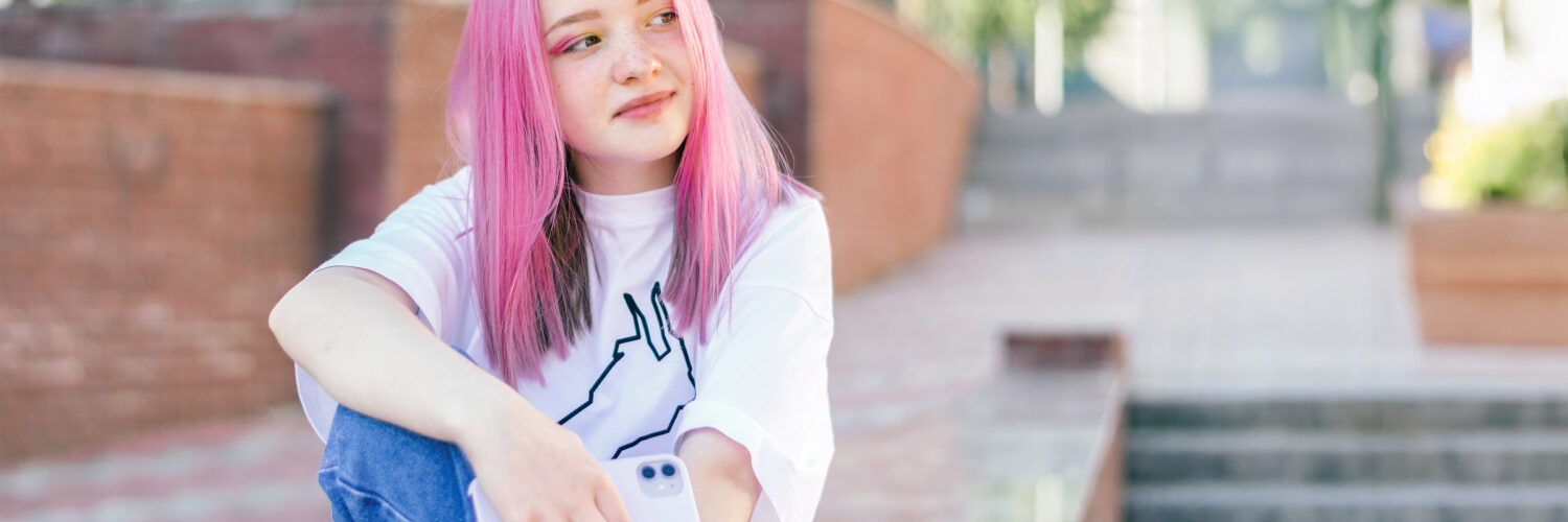 Pinkkihiuksinen tyttö istumassa ulkona kivetyllä tasanteella.