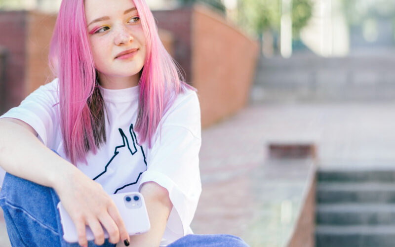 Pinkkihiuksinen tyttö istumassa ulkona kivetyllä tasanteella.