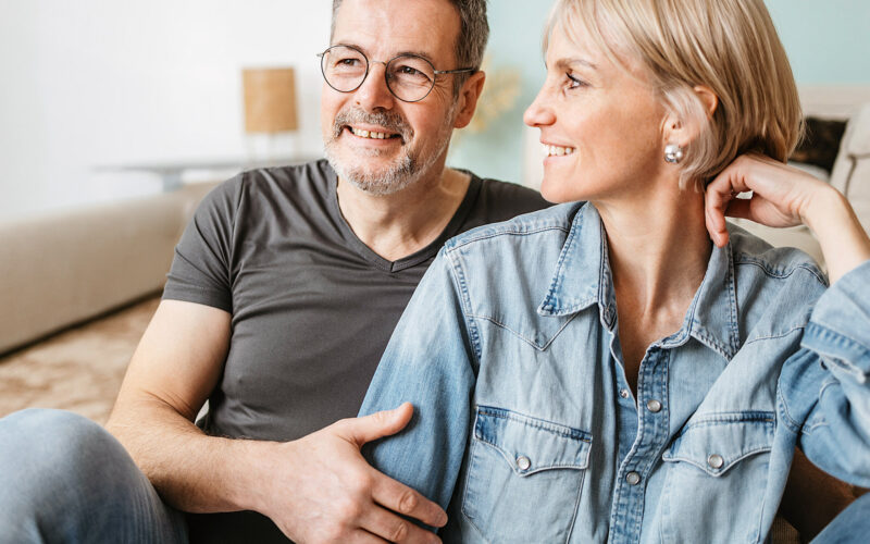 Keski-ikäinen pariskunta istuu sohvalla hymyillen.