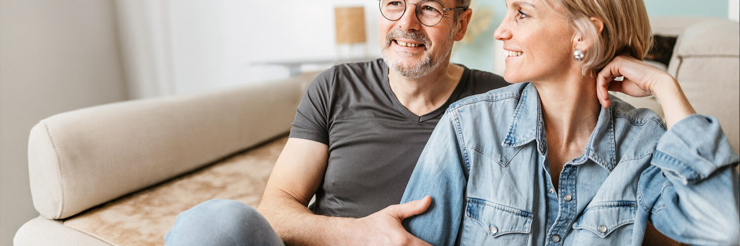 Keski-ikäinen pariskunta istuu sohvalla hymyillen.