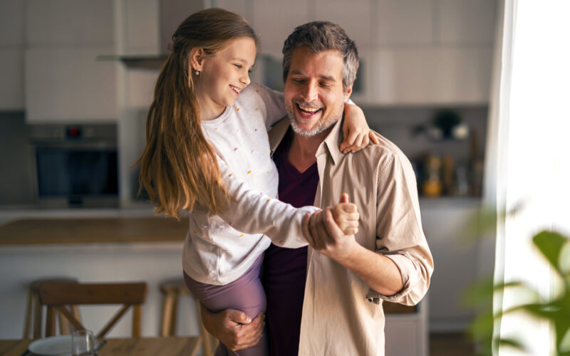 Tulehduksellista reumasairautta sairastava tyttö on isänsä sylissä ja he tanssivat keittiössä