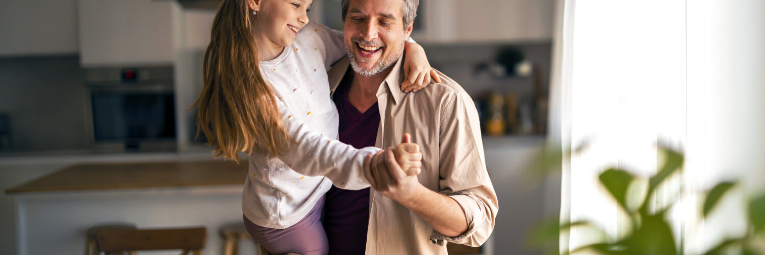 Tulehduksellista reumasairautta sairastava tyttö on isänsä sylissä ja he tanssivat keittiössä