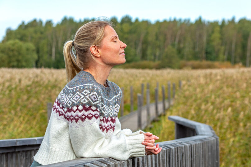 nainen ulkona silmät kiinni nojaa aitaan coronaria kuntoutuskurssi