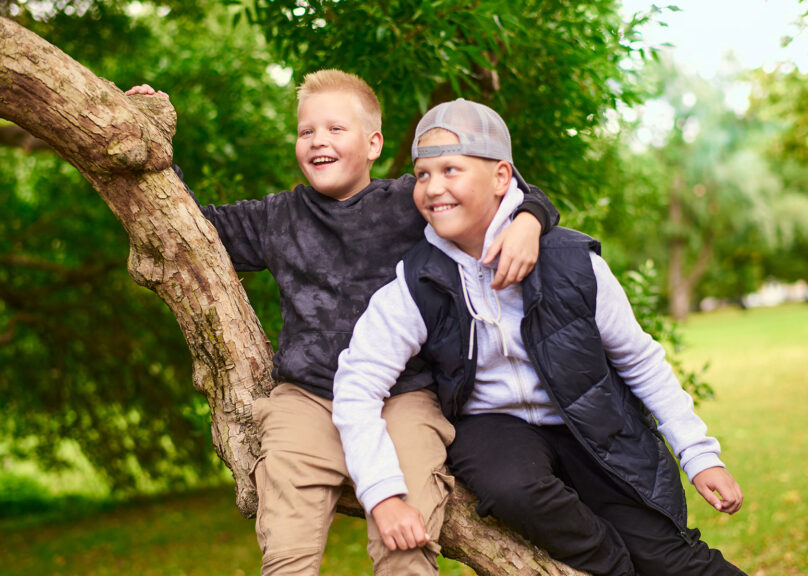 kaksi poikaa istuvat puun oksalla ja hymyilevät