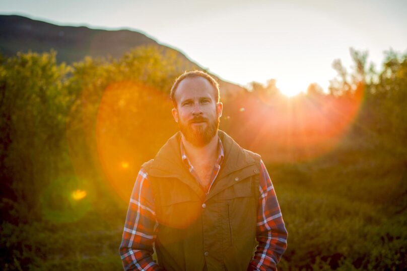 Mies seisoo ulkona ruska-aikaan ja katsoo kohti kameraa.