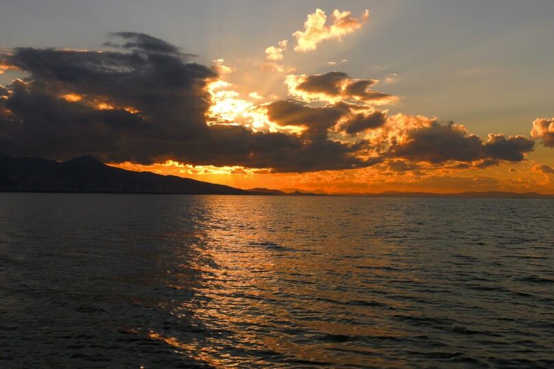 Meri ja horisontissa laskeva aurinko, tumma kuva.