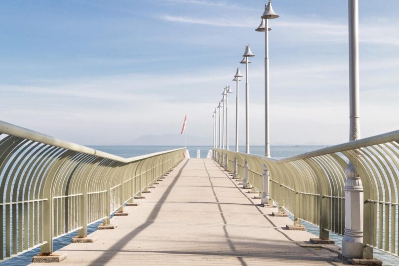 Silta ja katulamput suoraan edessä ja sillan päässä näkyy merenranta.