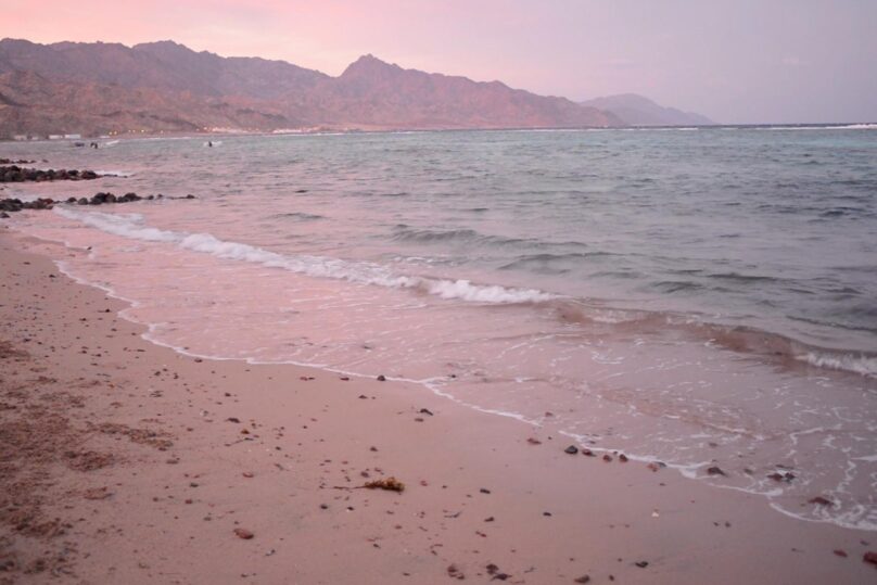 Punertava rantamaisema ja taustalla vuori.