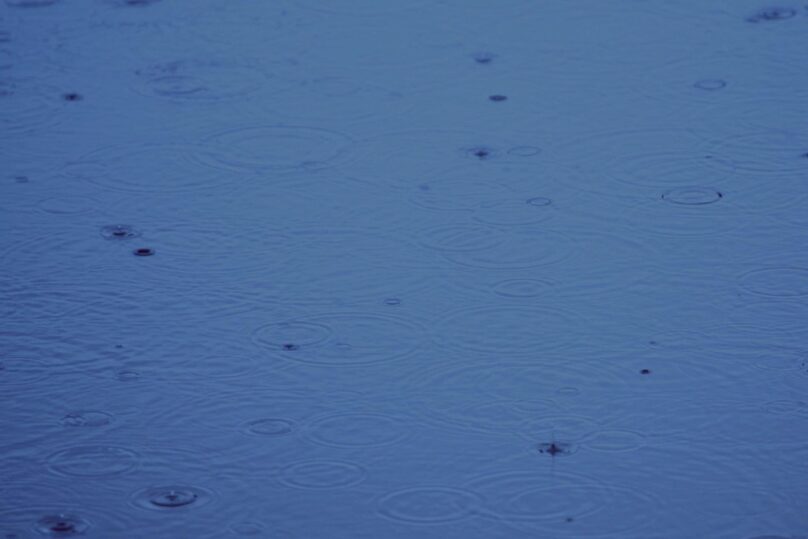 Tummansininen vedenpinta, jossa sadepisaroiden synnyttämiä renkaita.