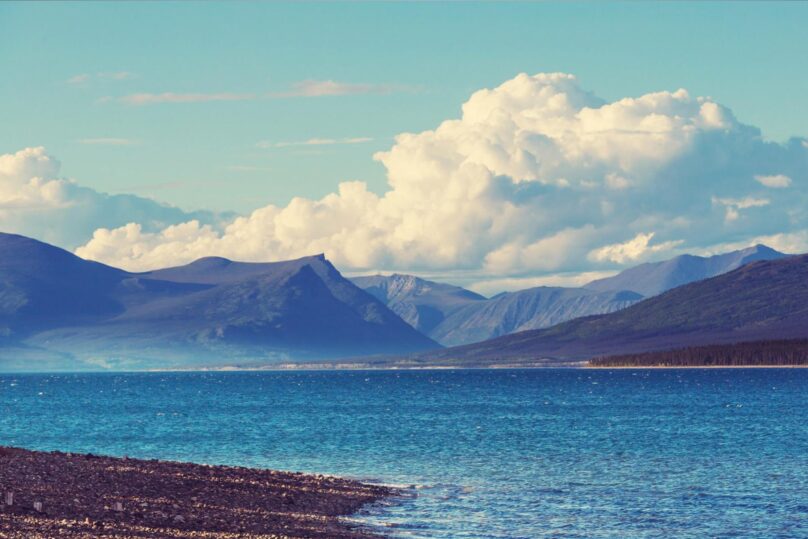 Merenrannalla ja vastapäätä tuntureita ja taustalla iso kumpupilvi.