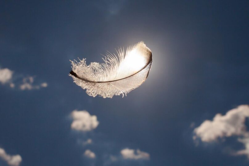 Yksi höyhen leijailee tummaa taivasta ja pilviä vasten.