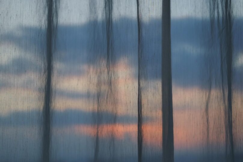 Punertava iltataivas verhojen läpi.