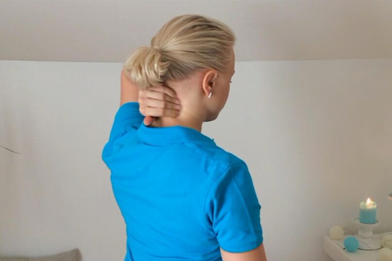 Sinipaitainen nainen kuvattuna takaapäin, kun hieroo kädellä niskaansa.