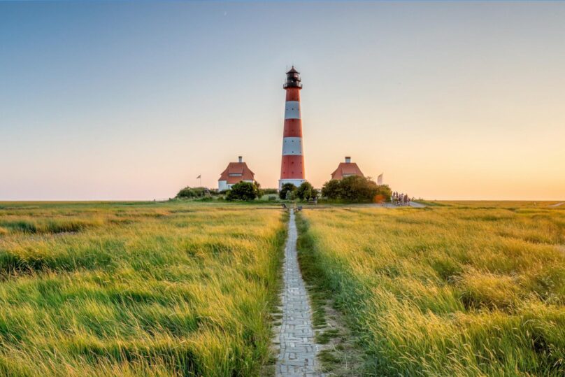 Punavalkoraidallinen majakka keskellä vihreää niittyä ja ilta-auringo paistaa.