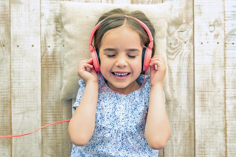 Tyttö kuuntelee kuulokkeista nauhoitetta silmät kiinni, puulattialle maaten.