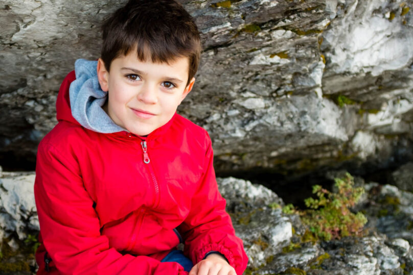 LAKU-perhekuntoutuksessa ollut poika istuu kalliolla punainen takki päällä