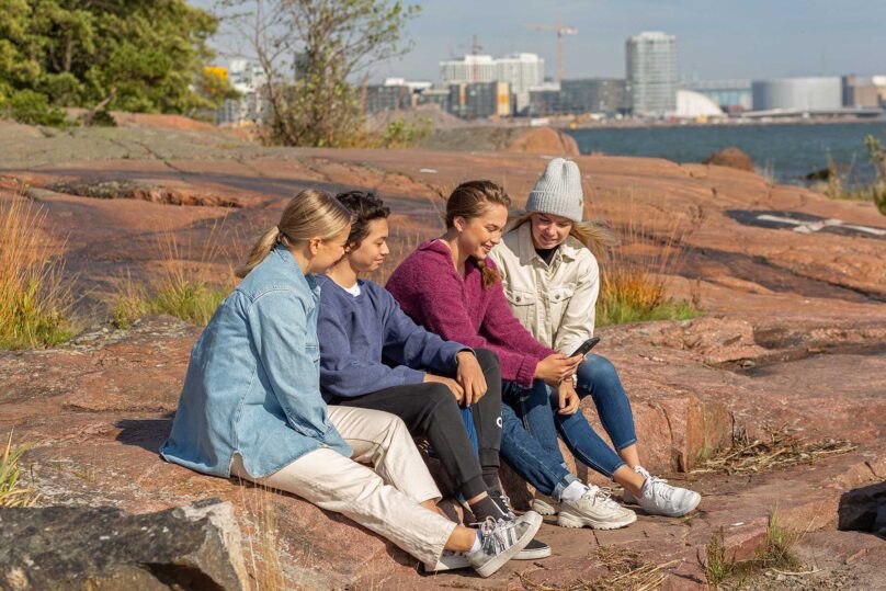 Neljä teini-ikäistä istuu kalliolla ja katsoo puhelinta