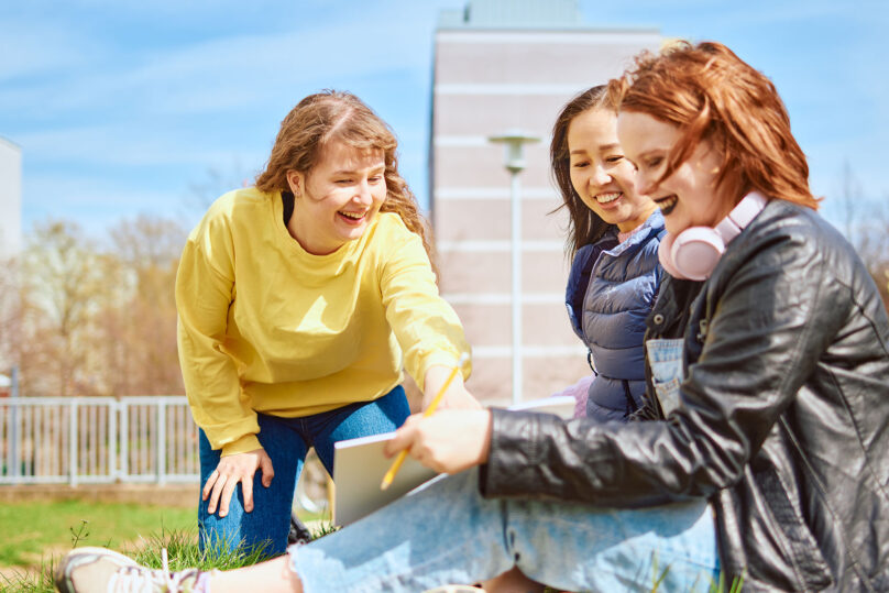 kolme nuorta naista hymyilevät ulkona