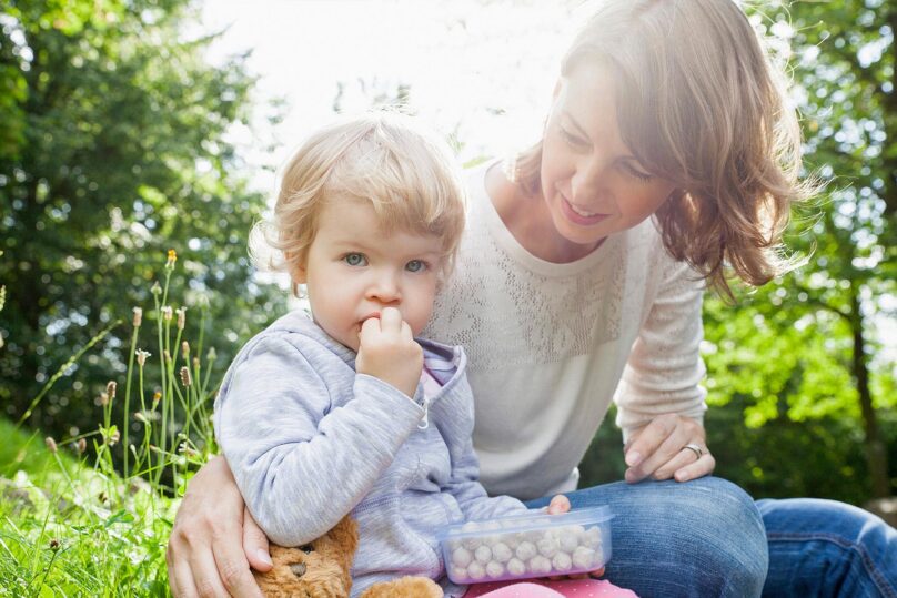 Pieni lapsi ja äiti ulkona kesällä. Lapsi katsoo kohti.