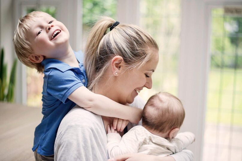 Nainen ja kaksi lasta hymyilevät sylikkäin sisätiloissa.