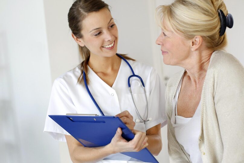Naislääkäri ja vanhempi nainen katsovat toisiaan hymyillen vastaanotolla.