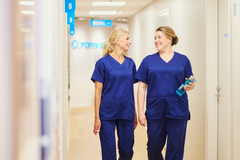 Hoitajat kävelevät käytävällä ja hymyilevät toisilleen.