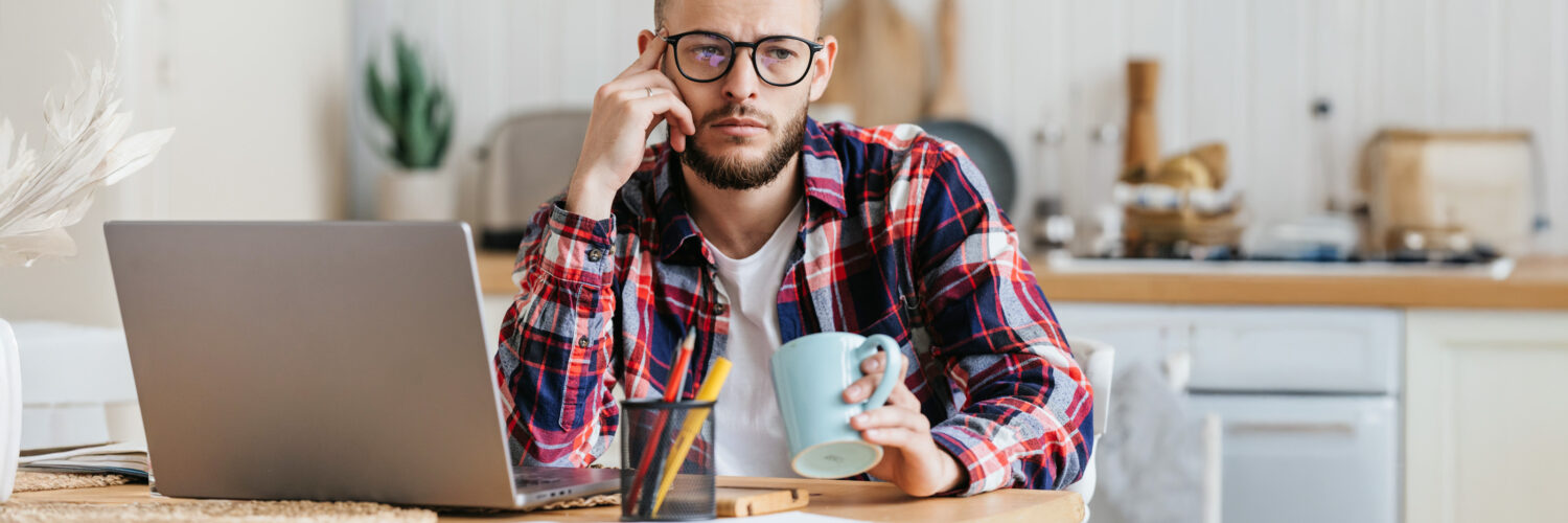 Mies istuu keittiössä apeana ja pohtivana läppärin edessä.