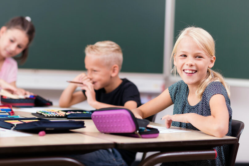 Lapset istuvat pöydän ääressä ja pöydällä on kyniä ja paperia.