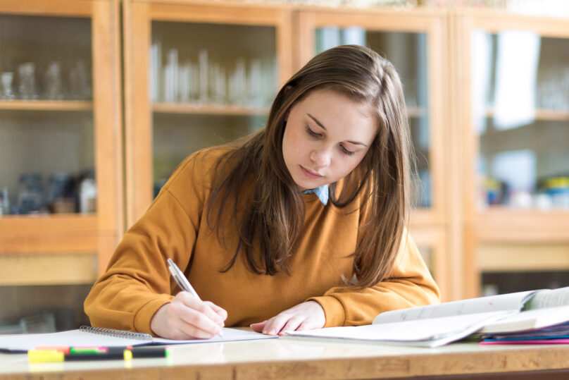Nuori tyttö kirjoittaa pöydän ääressä.
