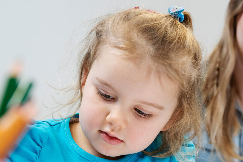 Lähikuvassa lapsi piirtämässä ja taustalla psykologi kirjaa merkintöjä paperille.