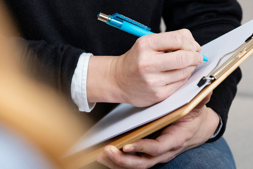 Lähikuva psykologin käsistä, kun hän kirjaa asioita paperille.