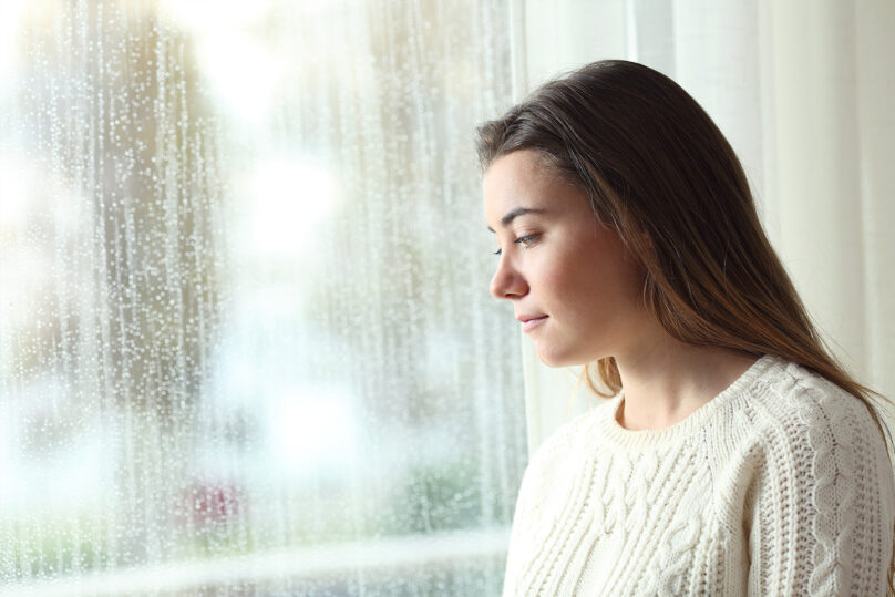 nuori nainen katsoo ulos sateisesta ikkunasta