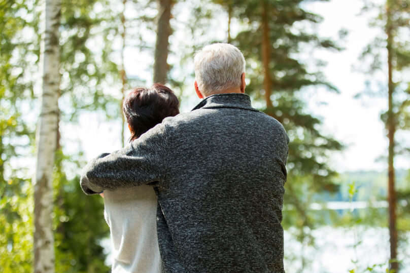 pariskunta seisoo vierekkäin ulkona ja katsovat yhdessä kohti vesimaisemaa