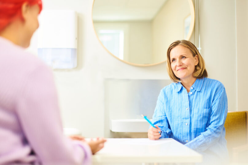 Vaaleahiuksinen ja kauluspaitainen asiantuntija keskustelee punatukkaisen asiakkaan kanssa,