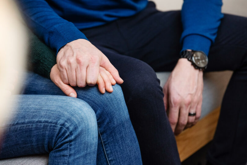 Lähikuva sohvalla istuvan pariskunnan käsistä.