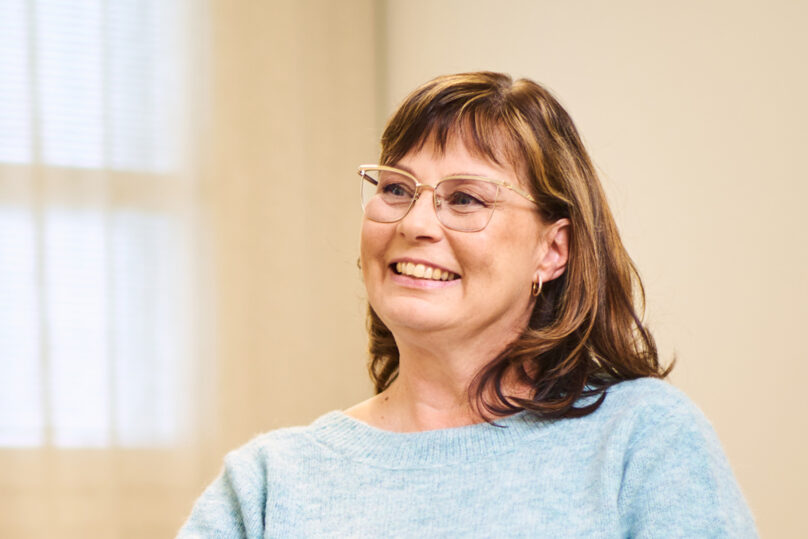 Tummahiuksinen naisasiakas hymyilee.