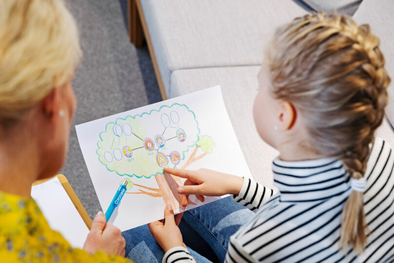 Terapeutti ja lapsiasiakas katsovat yhdessä piirustusta sukupuusta.